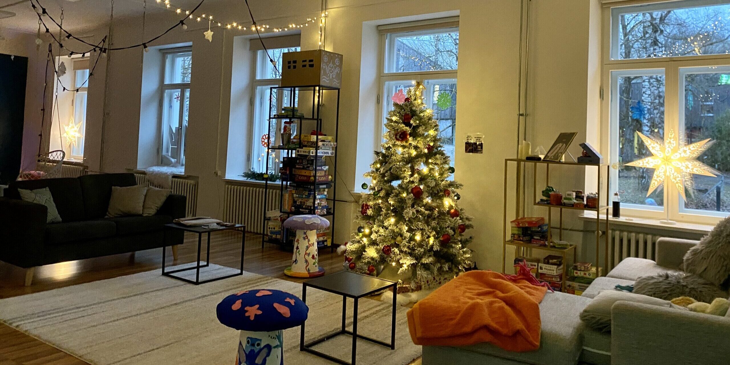 Jõuluootus Lillekese noortetoas (1) pildil on Lillekese noortekeskus, kus taamal särab jõulupuu, laes on jõulukaunistused, aknal särab jõulutäht. Diivanil on mõnusad pleedid, põrandal vaip. Kõik on õdus.