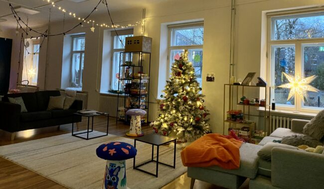 Jõuluootus Lillekese noortetoas (1) pildil on Lillekese noortekeskus, kus taamal särab jõulupuu, laes on jõulukaunistused, aknal särab jõulutäht. Diivanil on mõnusad pleedid, põrandal vaip. Kõik on õdus.